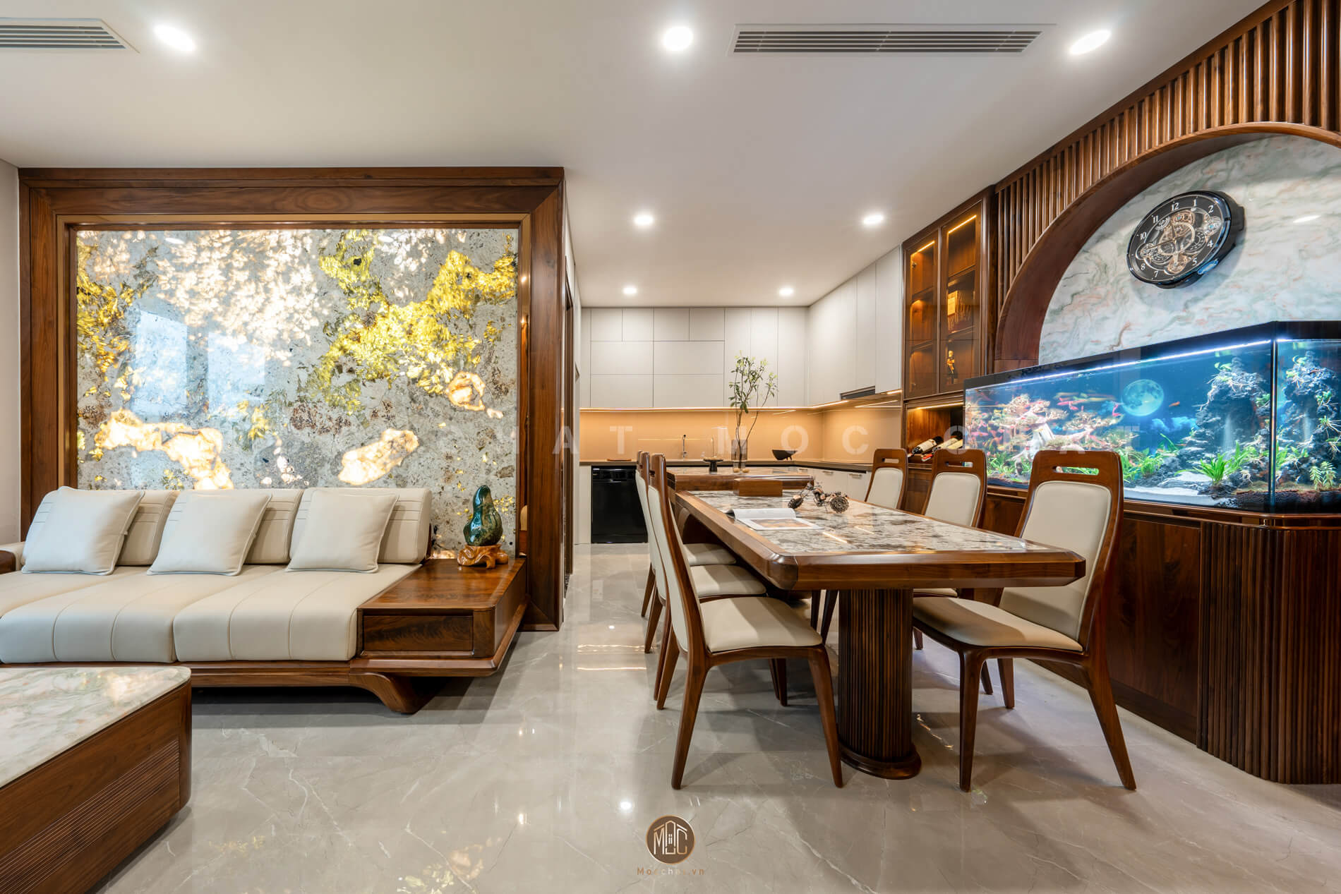 Không gian phòng khách liền phòng ăn sử dụng nội thất gỗ óc chó cao cấp, nổi bật với sofa gỗ óc chó, bàn ăn mặt đá marble và bể cá thủy sinh lớn, tạo sự sang trọng cho căn hộ hiện đại.